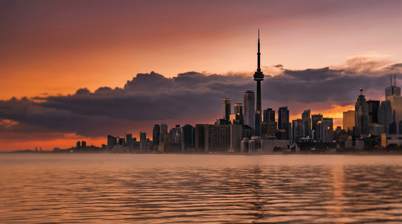 Aerial view of CN Tower at sunset with Toronto skyline and Lake Ontario waterfront, golden light and layered clouds